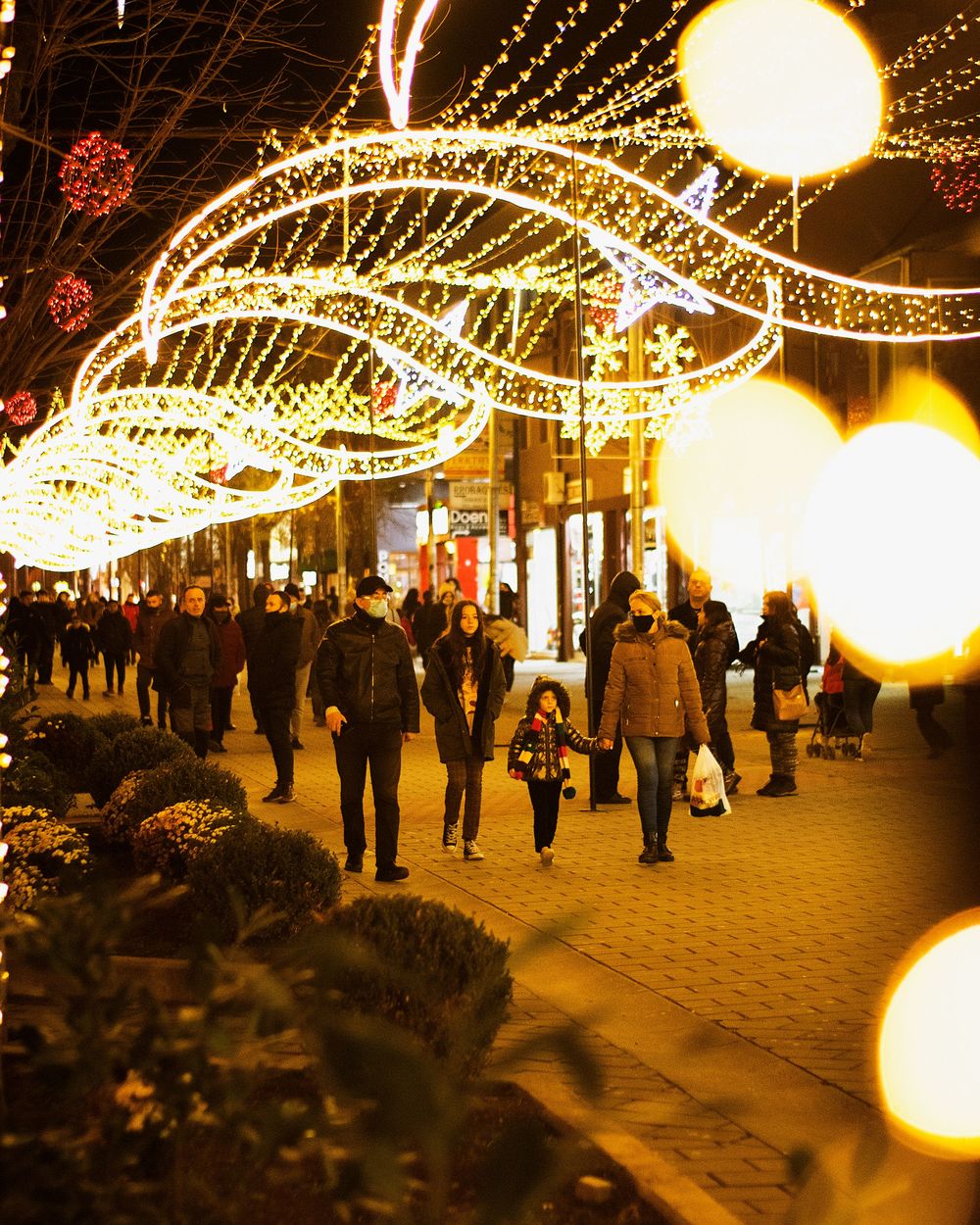 People walking under holiday light displays on a city street at night